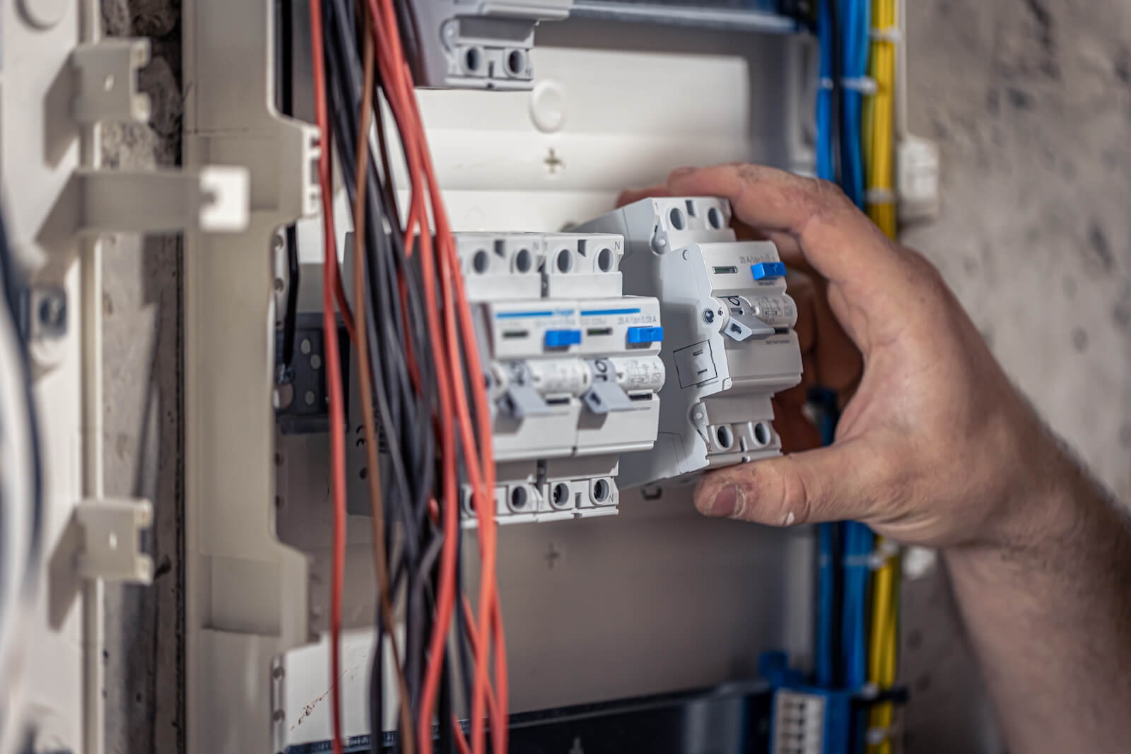 Dłoń elektryka montująca bezpiecznik w otwartej rozdzielnicy z kablami, urzeczywistniająca projekty techniczne instalacji elektrycznej.
